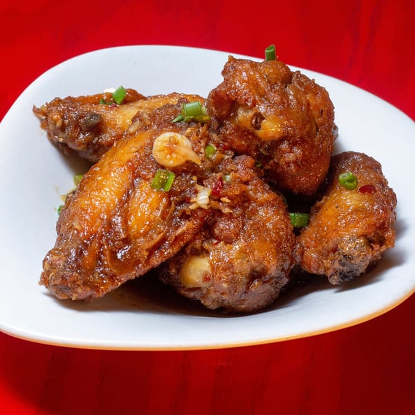 A white plate holds several glistening Asian chicken wings garnished with green onions and garlic.