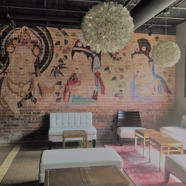 Lounge area with white couches, wooden tables, and a brick wall mural depicting Asian figures.