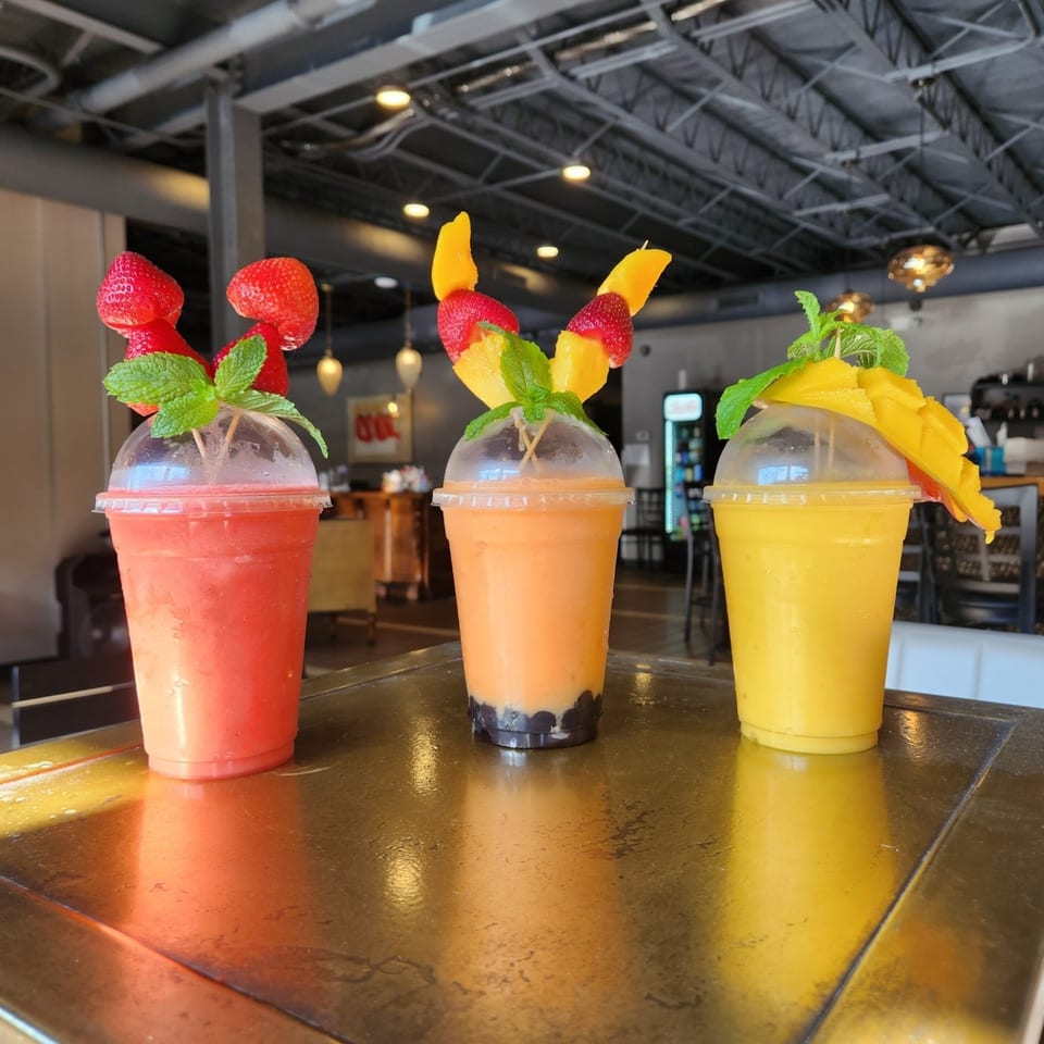 Three vibrant fruit smoothies, garnished with fresh fruit and mint, sit on a counter at Heavenly Asian Cuisine.