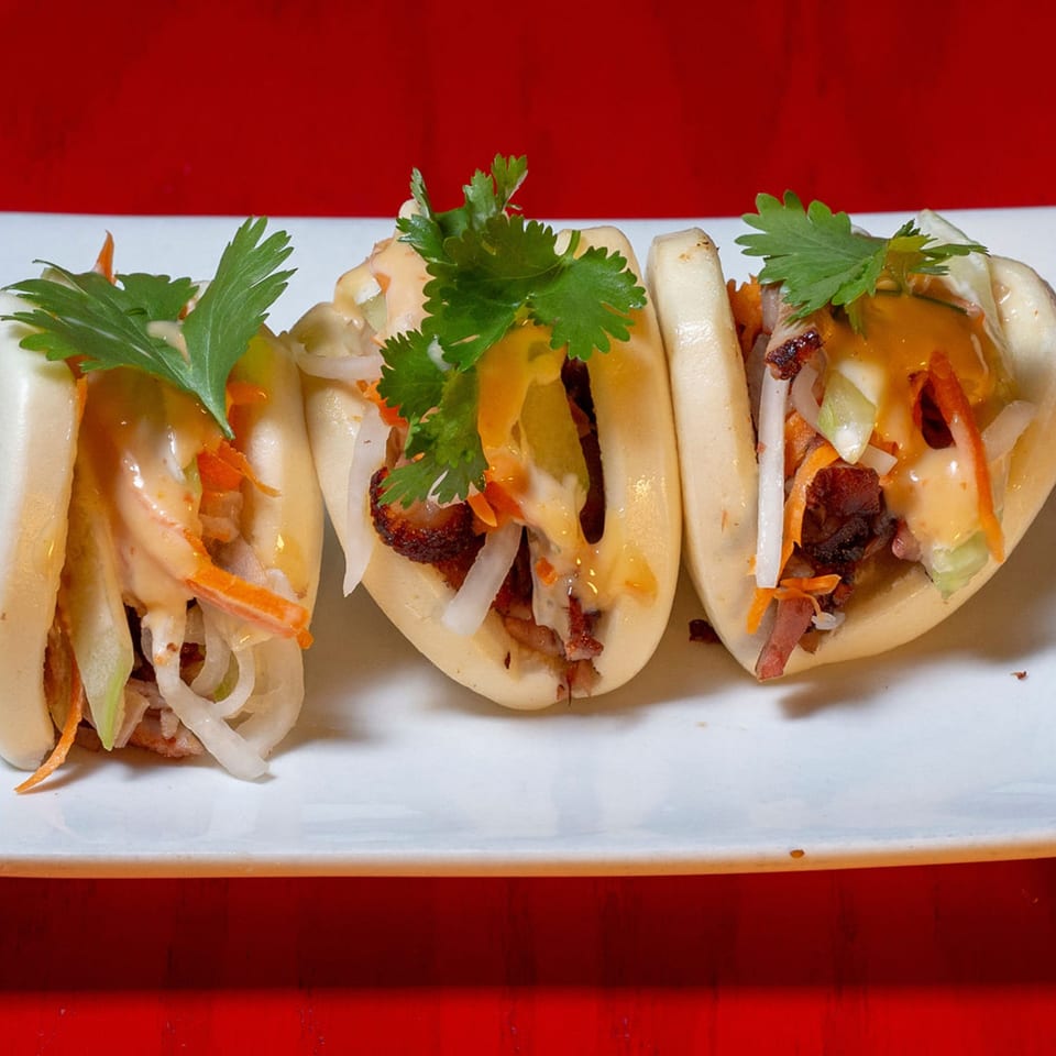 Three Heavenly Asian Cuisine bao buns filled with meat, vegetables, and sauce, garnished with cilantro.