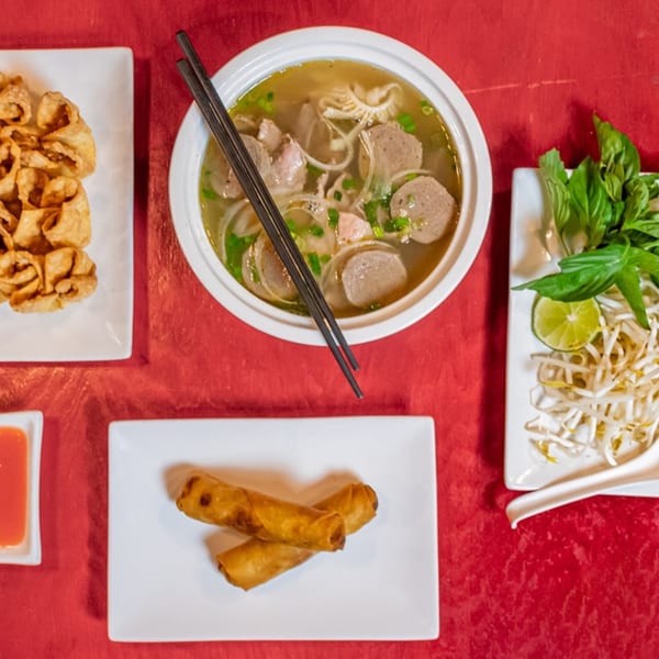 Overhead view of pho, fried wontons, spring rolls, and a side of basil, bean sprouts, and lime.