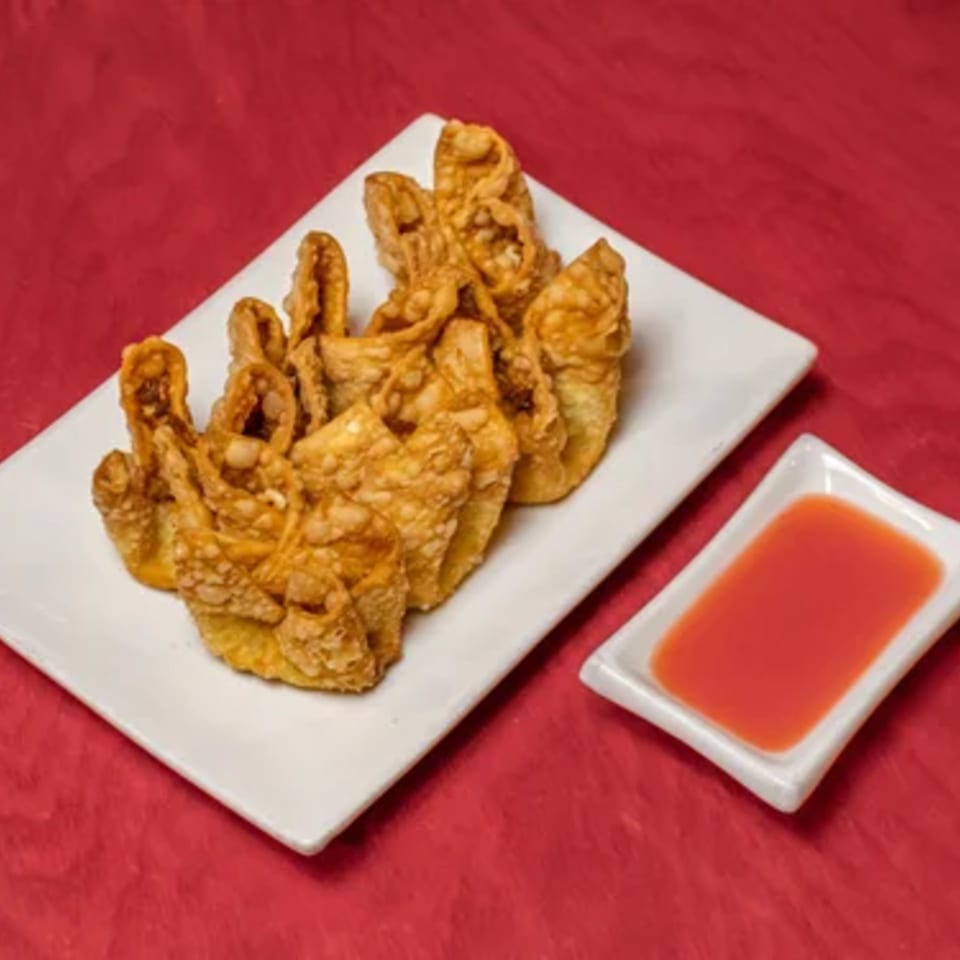 Crispy fried wontons on a white rectangular plate with a side of sweet chili dipping sauce.