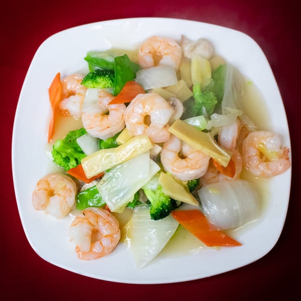 Shrimp with mixed vegetables, including broccoli, carrots, and cabbage, in a light sauce on a white plate.