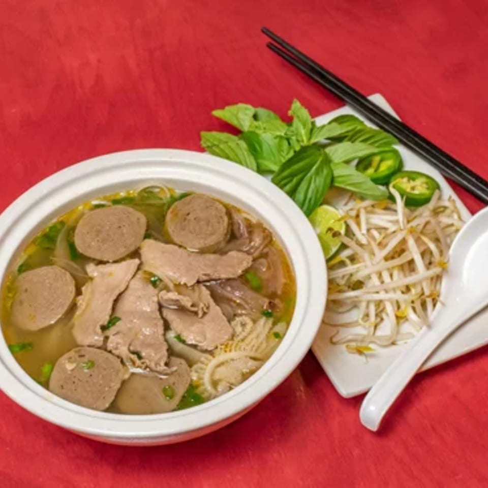 A bowl of Heavenly Asian Cuisine & Lounge's pho with beef, meatballs, and tripe, served with fresh herbs.