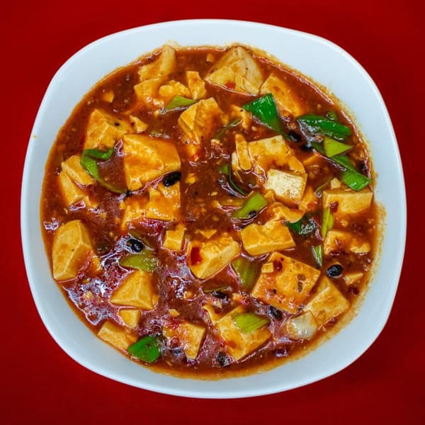 A white bowl filled with Heavenly Asian Cuisine's Mapo Tofu, featuring tofu cubes in a spicy red sauce.