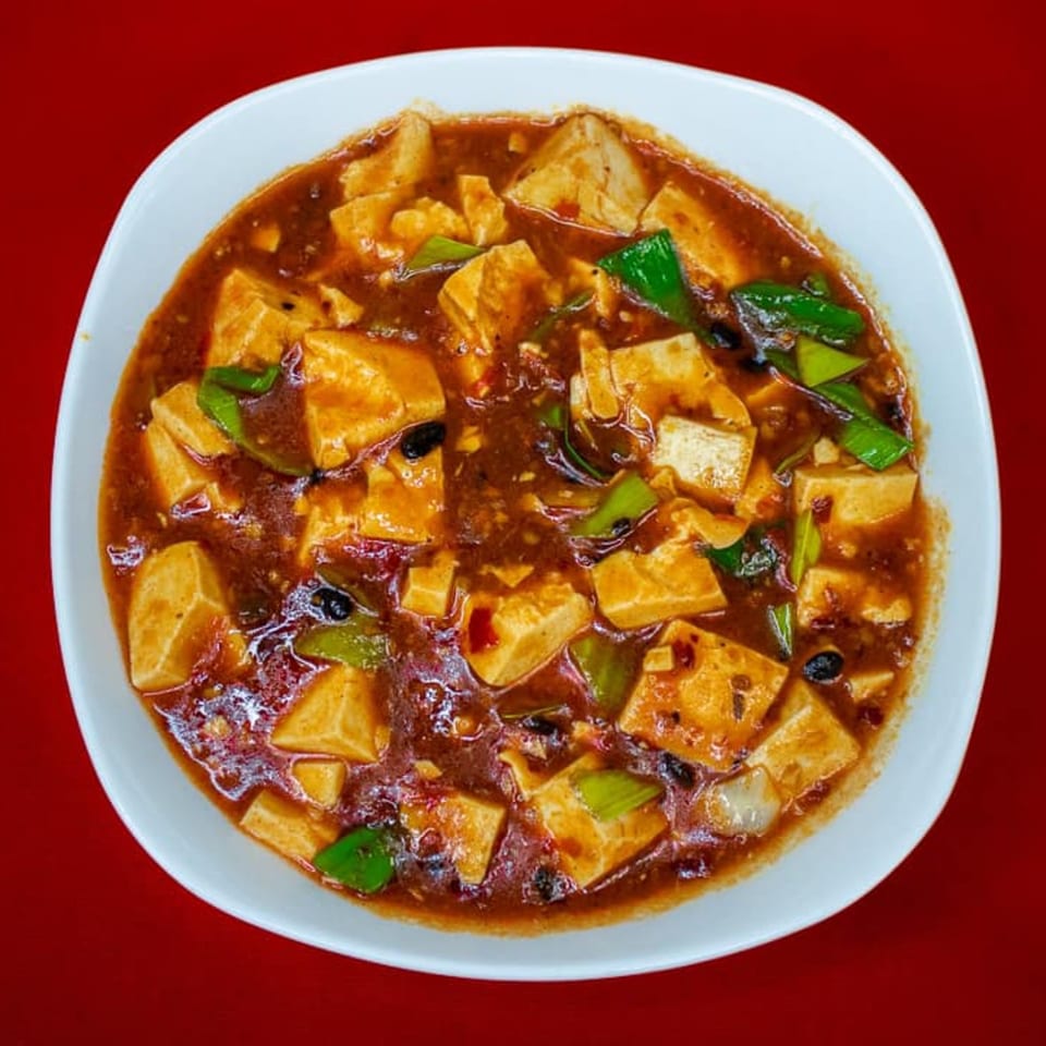 A white bowl filled with Heavenly Asian Cuisine's Mapo Tofu, featuring tofu cubes in a spicy red sauce.