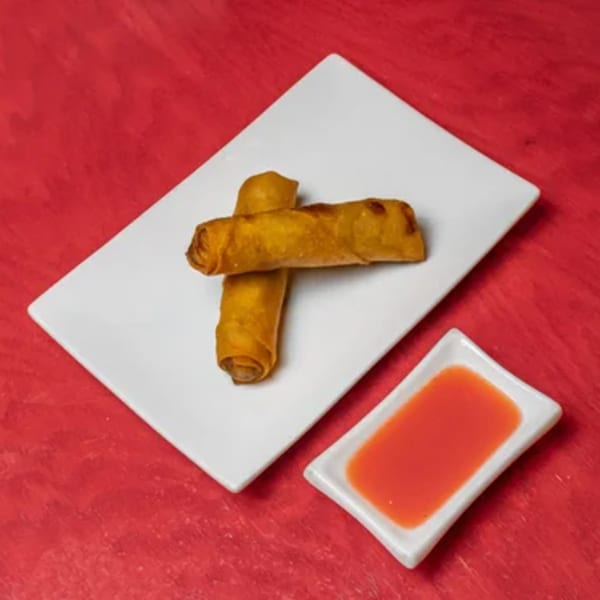 Two crispy golden spring rolls on a white rectangular plate with a side of sweet chili sauce.
